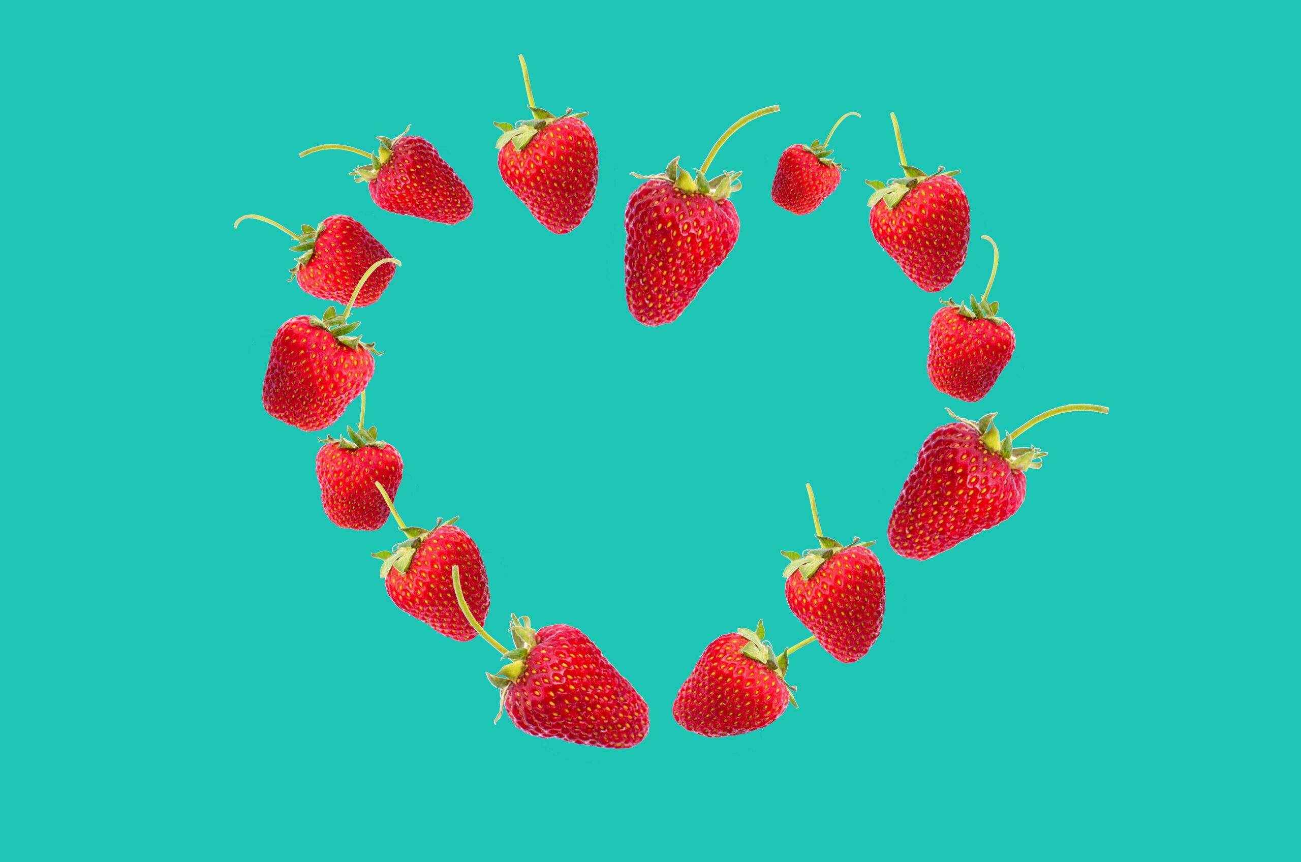 Vibrant red strawberries arranged in a heart shape on a bright turquoise background showcasing freshness and love.